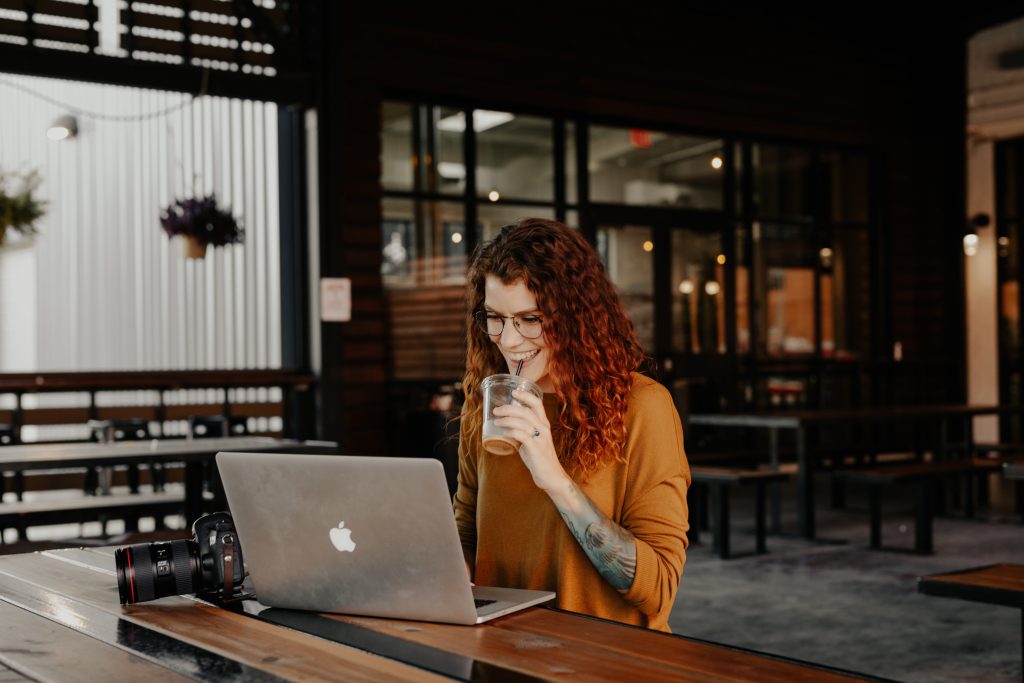 A girl sipping a drink and looking into a MacBook laptop