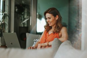 Woman in orange sleeveless top sitting on a couch in front of an open laptop