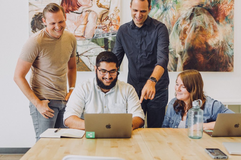 three men and a woman looking into a MacBook laptop