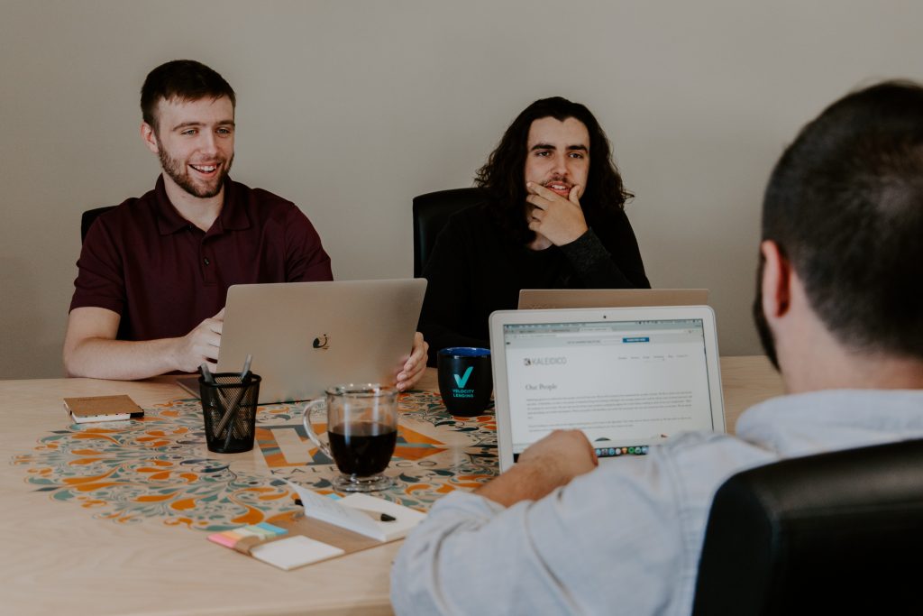 Three men sitting around a table using MacBooks