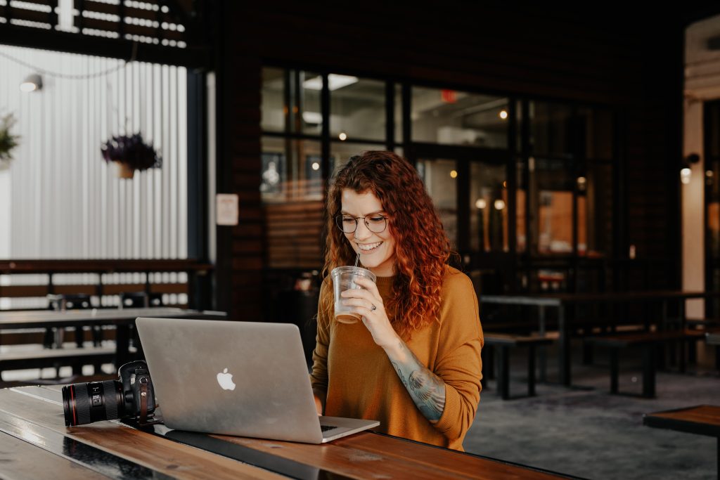 Woman in brown long sleeve shirt sitting beside a table using a MacBook.