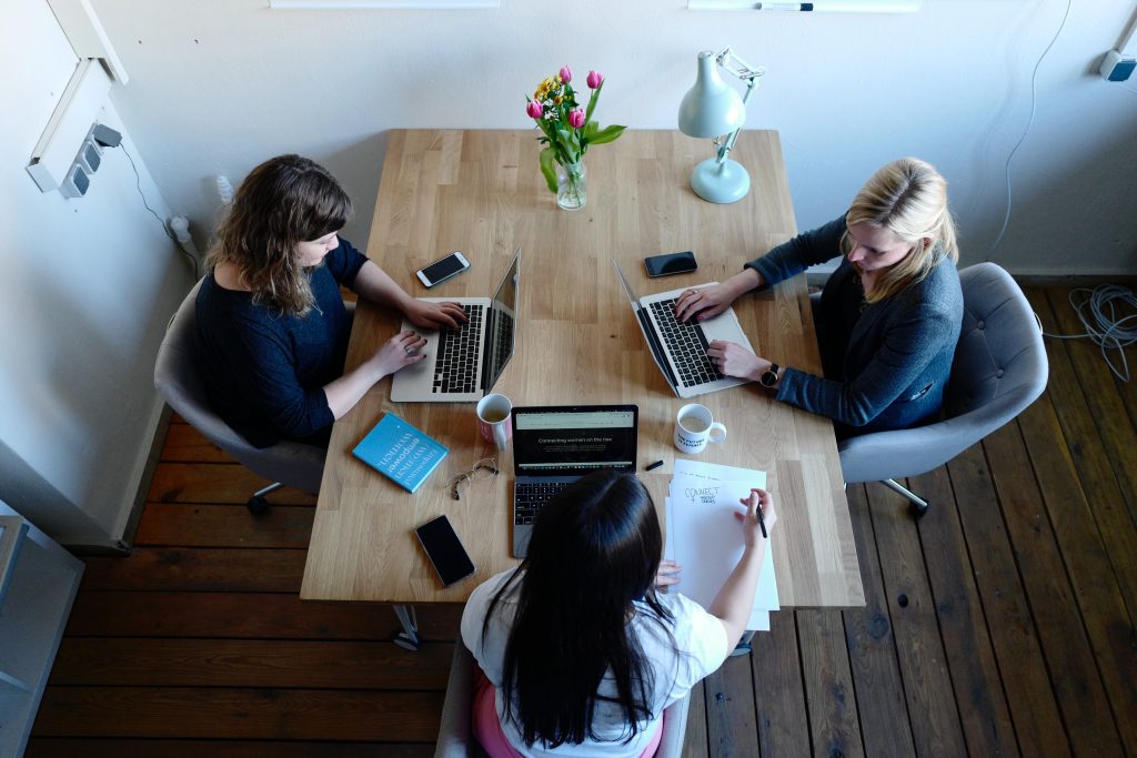 Three women sitting around a table using laptops