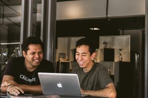 Two smiling men looking at a MacBook