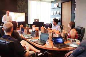 Man standing in front of people sitting beside table with open laptops