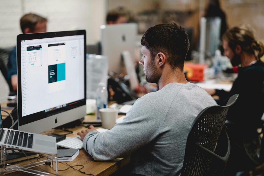 Man in grey sweatshirt sitting on chair in front of iMac